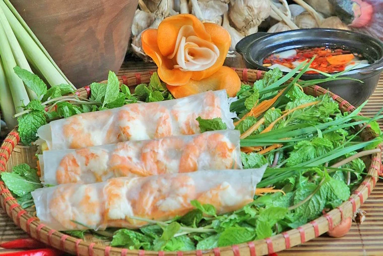 Nem Cuốn tôm : Fresh spring rolls with Prawns; An iconic appetizer in the refined culinary culture of Hanoi, these fresh spring rolls are a quintessential starter for festive family gatherings and cheerful reunions among friends. Beautifully handcrafted, the dish highlights fresh, succulent boiled shrimp, peeled and rolled alongside soft rice vermicelli, crisp cucumber, sweet pineapple, bright carrots, and a vibrant bouquet of fresh local herbs. The dish truly comes alive with its delicate dipping sauce—a finely balanced blend of fragrant fish sauce, minced garlic, and fresh chili, softened by the subtle sweetness of banana vinegar, a squeeze of fresh lime, and a gentle touch of sugar for a crisp, refreshing finish. • Key Ingredients: Fresh boiled shrimp, rice vermicelli, pineapple, cucumber, carrot, fresh herbs, rice paper. • Flavor Profile: Fresh and crisp with natural sweetness from seafood and fruit, balanced by an aromatic, sweet-and-sour garlic-chili dipping sauce.