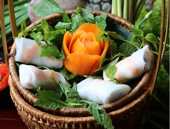Nem Cuốn tôm : Fresh spring rolls with Prawns; An iconic appetizer in the refined culinary culture of Hanoi, these fresh spring rolls are a quintessential starter for festive family gatherings and cheerful reunions among friends. Beautifully handcrafted, the dish highlights fresh, succulent boiled shrimp, peeled and rolled alongside soft rice vermicelli, crisp cucumber, sweet pineapple, bright carrots, and a vibrant bouquet of fresh local herbs. The dish truly comes alive with its delicate dipping sauce—a finely balanced blend of fragrant fish sauce, minced garlic, and fresh chili, softened by the subtle sweetness of banana vinegar, a squeeze of fresh lime, and a gentle touch of sugar for a crisp, refreshing finish. • Key Ingredients: Fresh boiled shrimp, rice vermicelli, pineapple, cucumber, carrot, fresh herbs, rice paper. • Flavor Profile: Fresh and crisp with natural sweetness from seafood and fruit, balanced by an aromatic, sweet-and-sour garlic-chili dipping sauce.